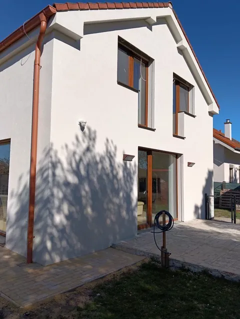 Biela fasáda rodinného domu s drevenými oknami a dlažbou pri vstupe