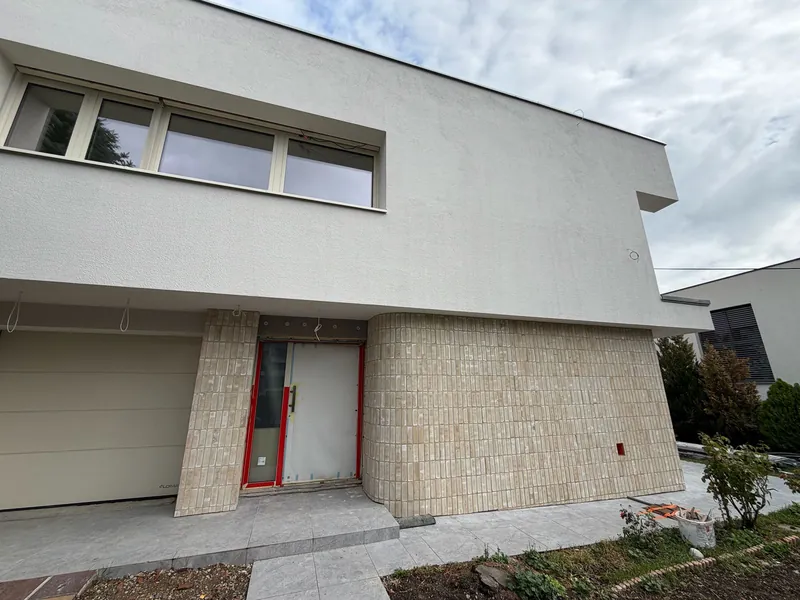 Vstup do domu s garážovou bránou a zaobleným rohom z tehlového obkladu