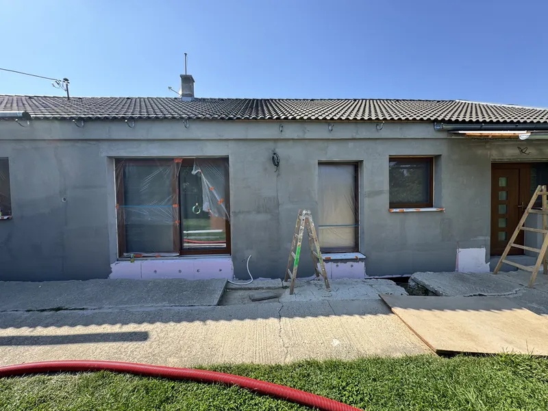 Starší rodinný dom s novou výstužnou vrstvou na fasáde a oknami zakrytými fóliou